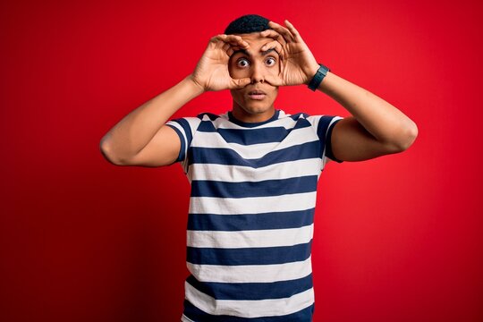 Handsome african american man wearing casual striped t-shirt standing over red background Trying to open eyes with fingers, sleepy and tired for morning fatigue