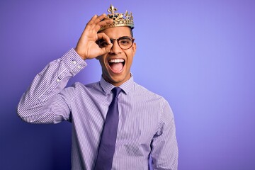 Young handsome african american man wearing golden crown of king over purple background doing ok gesture with hand smiling, eye looking through fingers with happy face.