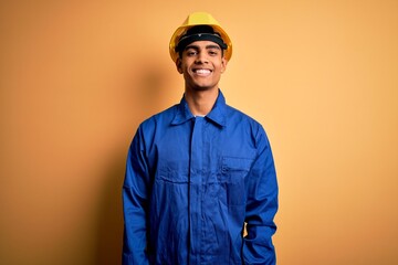 Young handsome african american worker man wearing blue uniform and security helmet with a happy...