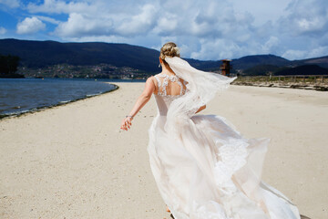Fototapeta na wymiar bride in a white wedding dress runs on the sand to the ocean, wedding day, girl having fun, rear view, beautiful spanish landscape