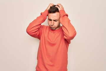 Young handsome man with blue eyes wearing casual sweater standing over white background suffering from headache desperate and stressed because pain and migraine. Hands on head.