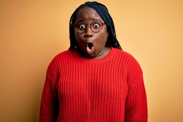 African american plus size woman with braids wearing casual sweater over yellow background afraid and shocked with surprise expression, fear and excited face.