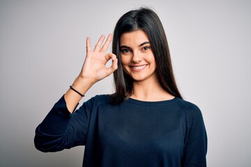 Young beautiful brunette woman wearing casual sweater standing over white background smiling positive doing ok sign with hand and fingers. Successful expression.