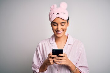 Young beautiful woman wearing pajama and sleep mask having conversation using smartphone with a happy face standing and smiling with a confident smile showing teeth