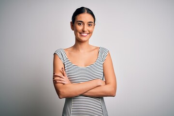 Obraz premium Young beautiful brunette woman wearing casual striped dress over isolated white background happy face smiling with crossed arms looking at the camera. Positive person.
