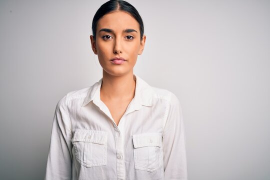 Young beautiful brunette woman wearing casual shirt over isolated white background with serious expression on face. Simple and natural looking at the camera.