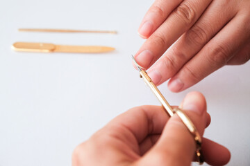 The woman is cutting her nails with small scissors by herself in close up photo on white background. View from above. Manicure at home