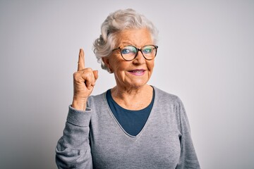 Senior beautiful grey-haired woman wearing casual sweater and glasses over white background pointing finger up with successful idea. Exited and happy. Number one.