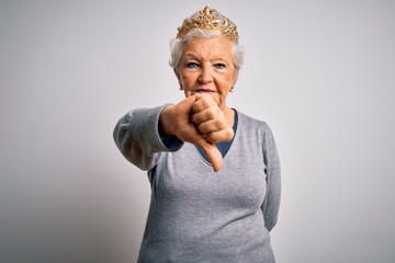 Senior beautiful grey-haired woman wearing golden queen crown over white background looking unhappy and angry showing rejection and negative with thumbs down gesture. Bad expression.