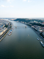 Obraz premium Aerial view of Széchenyi Chain Bridge over Danube river near Parliament palace in Budapest city, Hungary. Cars drive on bridge, road, boats floating on river, ships moored near riverside. Historic cen