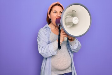 Young beautiful redhead speaker woman pregnant. Standing  screaming news using megaphone over isolated purple background