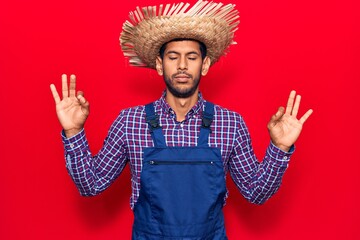 Young latin man wearing farmer hat and apron relax and smiling with eyes closed doing meditation gesture with fingers. yoga concept.