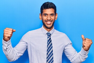 Young latin man wearing business clothes screaming proud, celebrating victory and success very excited with raised arms