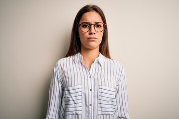 Young beautiful brunette woman wearing casual shirt and glasses over white background skeptic and...