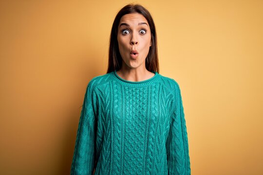 Young beautiful brunette woman wearing green casual sweater over yellow background afraid and shocked with surprise expression, fear and excited face.