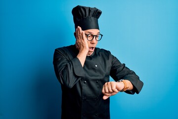 Middle age handsome grey-haired chef man wearing cooker uniform and hat Looking at the watch time worried, afraid of getting late