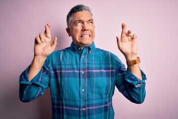 Naklejka premium Middle age handsome grey-haired man wearing casual shirt over isolated pink background gesturing finger crossed smiling with hope and eyes closed. Luck and superstitious concept.