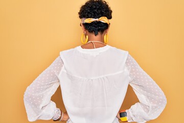 Young beautiful african american afro hippie woman wearing sunglasses and accessories standing backwards looking away with arms on body