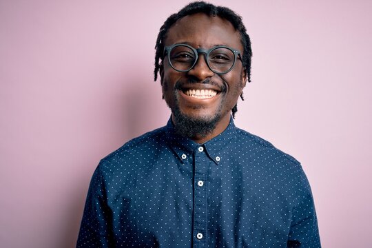 Young handsome african american man wearing casual shirt and glasses over pink background with a happy and cool smile on face. Lucky person.