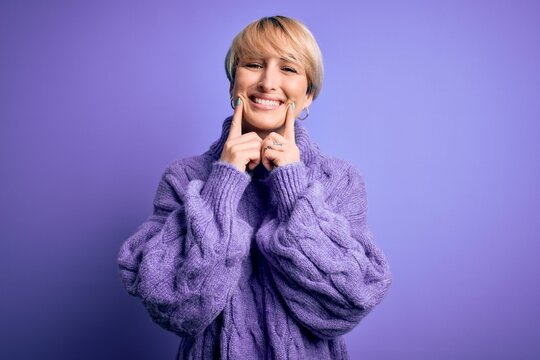 Young blonde woman with short hair wearing winter turtleneck sweater over purple background Smiling with open mouth, fingers pointing and forcing cheerful smile