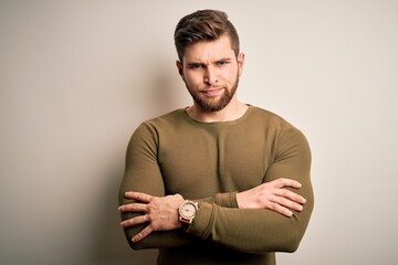 Young blond man with beard and blue eyes wearing green sweater over white background skeptic and nervous, disapproving expression on face with crossed arms. Negative person.
