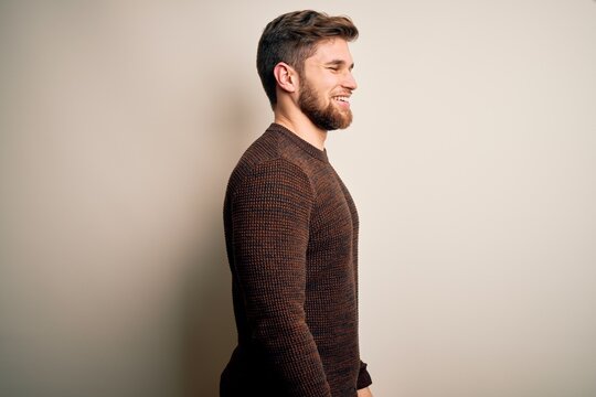 Young handsome blond man with beard and blue eyes wearing casual sweater standing looking to side, relax profile pose with natural face with confident smile.