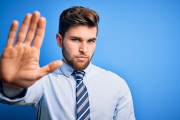 Young blond businessman with beard and blue eyes wearing elegant shirt and tie standing doing stop sing with palm of the hand. Warning expression with negative and serious gesture on the face.