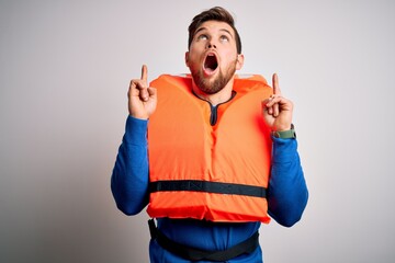 Young blond tourist man with beard and blue eyes wearing lifejacket over white background amazed...