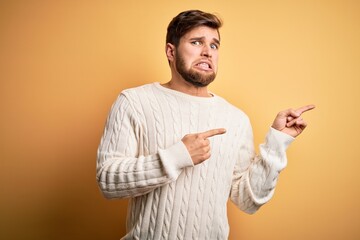 Young blond man with beard and blue eyes wearing white sweater over yellow background Pointing aside worried and nervous with both hands, concerned and surprised expression