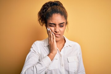 Young beautiful african american girl wearing casual shirt standing over yellow background touching mouth with hand with painful expression because of toothache or dental illness on teeth. Dentist