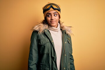Young african american afro skier girl wearing snow sportswear and ski goggles smiling looking to the side and staring away thinking.