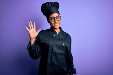 Young african american chef girl wearing cooker uniform and hat over purple background showing and pointing up with fingers number five while smiling confident and happy.