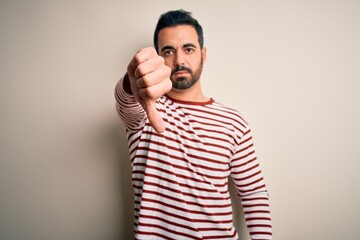 Young handsome man with beard wearing casual striped t-shirt standing over white background looking unhappy and angry showing rejection and negative with thumbs down gesture. Bad expression.