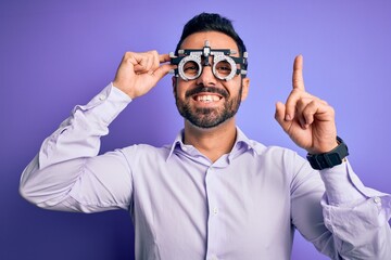 Young handsome optical man with beard wearing optometry glasses over purple background surprised with an idea or question pointing finger with happy face, number one