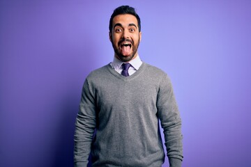 Handsome businessman with beard wearing casual tie standing over purple background sticking tongue out happy with funny expression. Emotion concept.