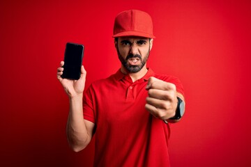 Young handsome delivery man with beard holding smartphone showing deliver food app annoyed and frustrated shouting with anger, crazy and yelling with raised hand, anger concept