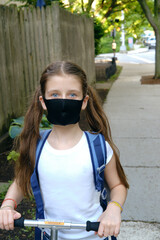 Elementary school student in a cloth dust mask with backpack. Preteen girl is riding scooter to or from school in new normal. Education, coronavirus, back to school, second wave, hybrid mode concept