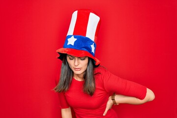 Young beautiful brunette woman wearing united states hat celebrating independence day Suffering of backache, touching back with hand, muscular pain