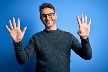 Young handsome man wearing casual sweater and glasses standing over blue background showing and...