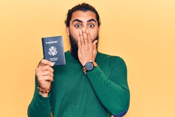 Young arab man holding united states passport covering mouth with hand, shocked and afraid for...