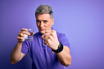 Young modern man drinking a glass of fresh water over purple isolated background annoyed and frustrated shouting with anger, crazy and yelling with raised hand, anger concept