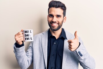 Young handsome man with beard drinking mug of coffe with best dad ever message smiling happy and positive, thumb up doing excellent and approval sign