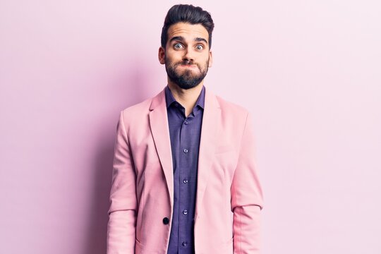 Young handsome man with beard wearing elegant jacket puffing cheeks with funny face. mouth inflated with air, crazy expression.