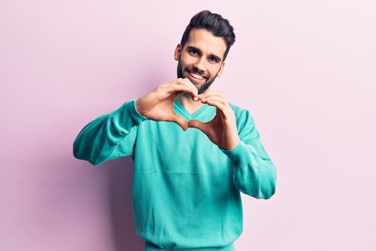 Young handsome man with beard wearing casual sweater smiling in love doing heart symbol shape with hands. romantic concept.