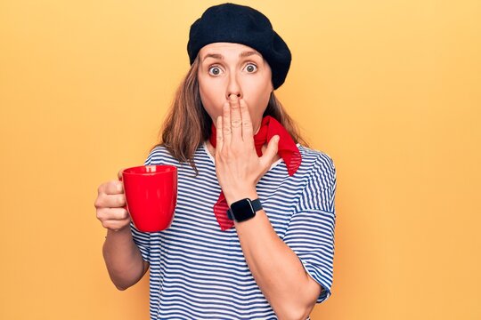 Young beautiful blonde woman wearing fashion beret drinking a cup of coffee covering mouth with hand, shocked and afraid for mistake. surprised expression