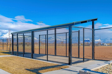 Baseball field dugout with slanted roof and chain link fence on a sunny day - obrazy, fototapety, plakaty