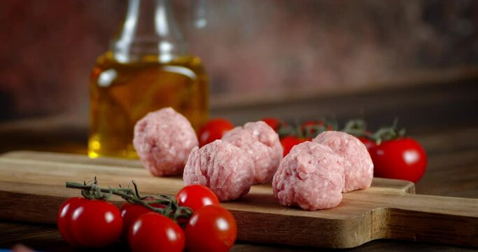 Male hand put raw meatballs on cutting Board with tomatoes.