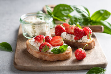 bruschettas with strawberries, cream cheese and basil on a wooden board on a light background