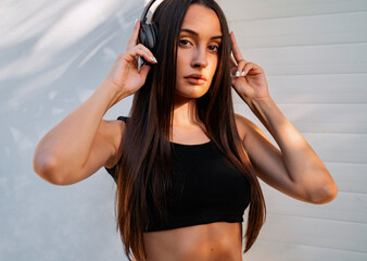 Attractive young adult with long hair, listening to music on headphones outdoors. Abstract shadows in background