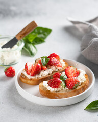 bruschettas with strawberries, cream cheese and basil in a white plate on a light background.